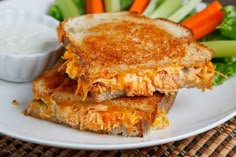 two grilled sandwiches on a white plate with carrots, celery and dip