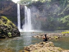 a person is sitting on rocks in front of a waterfall and looking at the water