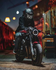 a man riding on the back of a motorcycle down a street at night with lights in the background