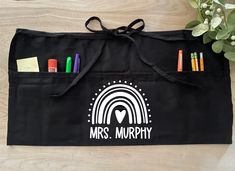 a black bag with markers and pencils in it sitting on a wooden table next to a potted plant