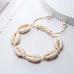 a white bracelet with shell beads and pearls on it's end, sitting on a table