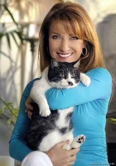 a woman holding a black and white cat in her arms while smiling at the camera