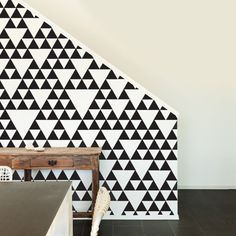 a black and white triangle wallpaper with a wooden table in the corner next to it