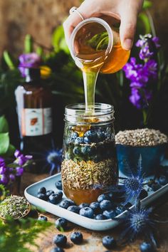 a person pouring honey into a jar filled with blueberries and other foodstuffs