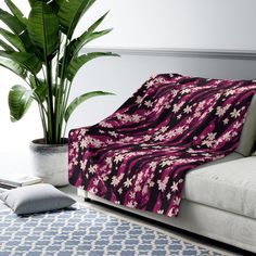 a pink and black blanket sitting on top of a couch next to a potted plant