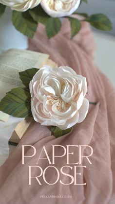 paper rose is laying on top of an open book, with leaves and flowers around it