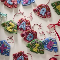 knitted christmas ornaments hanging from strings on a white surface with red and green ribbons