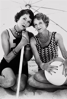 two women sitting under an umbrella on the beach posing for a photo with their arms around each other