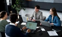 four people sitting around a table with laptops