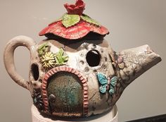 a ceramic teapot with a bird house on it's top and flowers in the roof