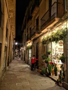 an alley way with people walking down the street at night and potted plants on either side