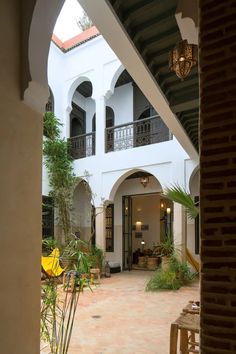 an open courtyard with potted plants and hanging lanterns on the ceiling, in front of a large white building