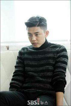 a man sitting on top of a white couch wearing a black and gray striped sweater