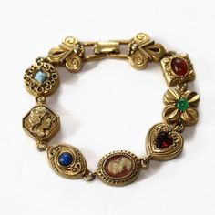 Vintage Victorian Revival Bracelet. This lovely bracelet features 7 different 'charms' including a cameo and heart, with the links on the ends featuring the flour de lis. Fold over clasp. Circa 1960's Marked: Goldette Measurements: 7" length Very good condition, minor wear due to age/use Vintage Jeweled Bracelets For Collectible, Vintage Cameo Metal Jewelry, Vintage Metal Cameo Jewelry, Vintage Cameo Bracelet Jewelry, Vintage Cameo Bracelet, Vintage Cabochon Bracelets, Vintage Cabochon Bracelets As Gift, Vintage Cabochon Bracelet Gift, Collectible Vintage Charm Costume Bracelets