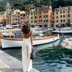 a woman standing on the edge of a dock next to some boats and buildings in the background