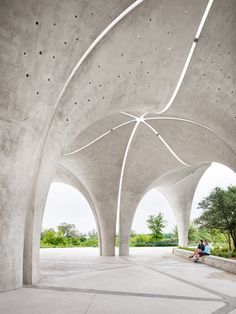 a person sitting on a bench under an overhang in a concrete structure with trees and bushes