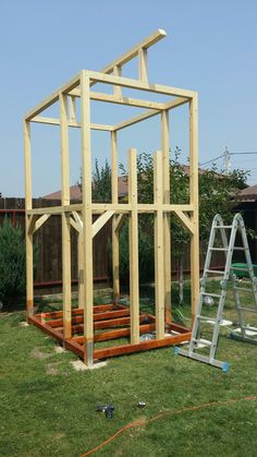 a wooden structure sitting on top of a lush green field next to a metal ladder