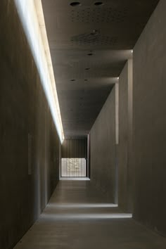 an empty hallway with light coming in from the ceiling and windows on both sides that lead to another room