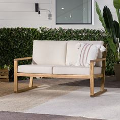 a white couch sitting on top of a wooden bench next to a green plant in front of a window