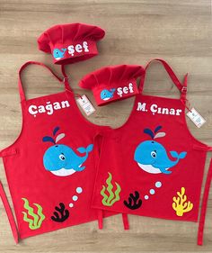 three children's aprons with matching hats and name tags on them, sitting on a wooden floor