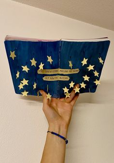 a hand holding an open book with stars on it