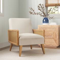 a white chair sitting in front of a window next to a vase with flowers on it