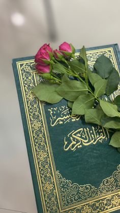 two roses are laying on top of a book that is open to read the koran