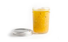 a glass jar filled with yellow liquid next to a metal lid on a white surface