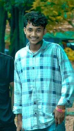 a young man standing in front of a tree with his hands in his pockets and smiling at the camera