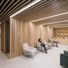 two people are sitting in chairs in an office with wooden slats on the walls