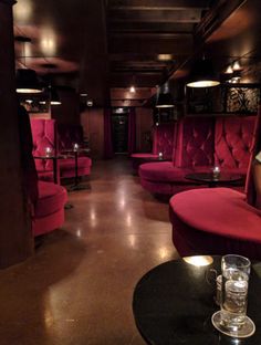 the interior of a restaurant with red velvet booths and tables, lit by candle lights