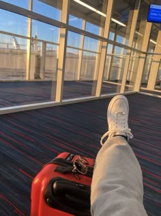 a person's feet resting on top of a red piece of luggage at an airport