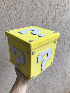 a hand is holding up a yellow box with question marks on the front and sides