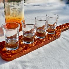 four shot glasses sitting on a tray next to a bottle of alcohol and some rocks