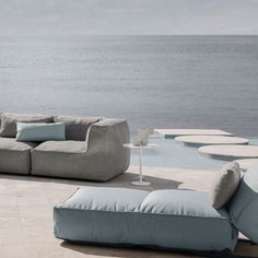 a couch sitting on top of a stone floor next to the ocean with pillows and lamps