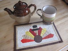 a table with a tea pot, mug and turkey place mat on top of it