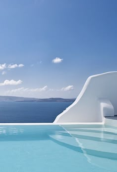 an outdoor swimming pool with blue water and white steps leading to the ocean, on a sunny day