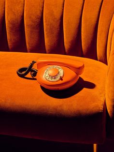 an orange phone sitting on top of a couch next to a corded telephone receiver