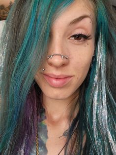 a woman with blue and green hair has piercings on her nose while she looks at the camera