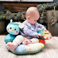 a baby playing with a stuffed animal on top of a cushion in front of potted plants