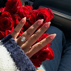 a woman's hand with a diamond ring on it next to red roses