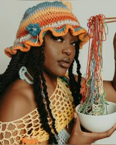 a woman wearing a crochet hat holding a bowl of yarn and looking at the camera