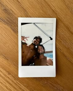 two men standing next to each other on top of a wooden table with a polaroid