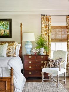 a bed room with a neatly made bed next to a dresser and a chair in front of a window