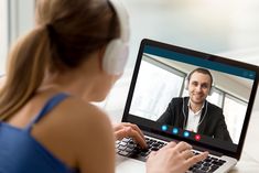 a woman sitting in front of a laptop computer with a man on it's screen