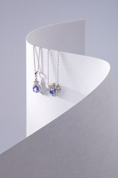 two silver necklaces with blue stones hanging from them on a white stand against a gray background