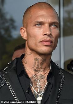 a man with tattoos on his neck and chest standing in front of a glass door