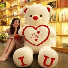 a woman sitting on the floor next to a giant teddy bear with i love u written on it