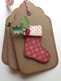 two tags with christmas decorations on them hanging from twine strings, one has a stocking and the other has a candy cane