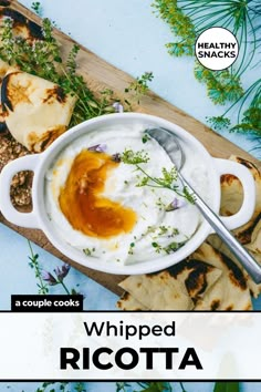 a white bowl filled with whipped ricotta next to pita bread and sprigs of herbs